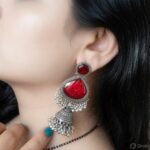 Woman wearing red stone silver jhumka earrings with intricate oxidised silver detailing